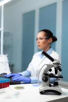 Selectiv focus on medical microscope standing on table in biochemistry hospital laboratory during experiment. Specialist microbiologist woman doctor working at biology experiment using biotechnology photo