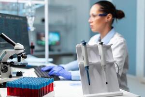 Chemist scientist woman with white coat discovering vaccine against virus typing medical expertise on computer. Professional modern equipment standing on table in hospital laboratory photo