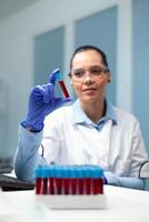 Scientist doctor woman analyzing transparent vacutainer with blood working at microbiology experiment in hospital laboratory. Biologist researcher developing medical vaccine against virus disease photo