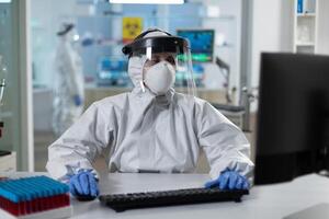 Scientist woman with protection medical equipment against covid19 typing covid19 test results working at vaccine development in scientific hospital laboratory. Virus prevention experiment photo