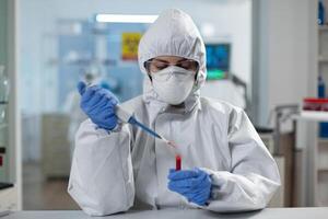 Scientist woman analyzing blood using medical micropippete during covid19 vaccine development working in microbiological hospital laboratory. Researcher wearing ppe suit during clinical experiment photo