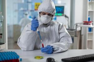 Scientist woman analyzing blood using medical micropippete during covid19 vaccine development working in microbiological hospital laboratory. Researcher wearing ppe suit during clinical experiment photo