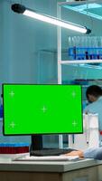 Microbiologist working on computer with display, green chroma key screen talking with coworker about new vacutainer with blood samples. Team of biotechnology scientists developing drugs. photo