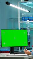 Doctor talking with lab technician and working with green mock-up screen desktop computer. Man lab researcher discussing with doctor about vaccine developent looking at blood samples photo