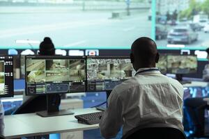 Observation room employee reviewing surveillance footage to find illegal activity within urban traffic, big screen. African american man collecting data via CCTV radar system. photo