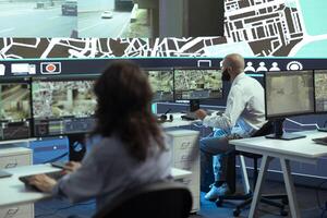 Diverse employees giving gps coordinates to couriers via satellite navigation, using city map to avoid traffic for express delivery service. Operators communicating routes for trucks. photo