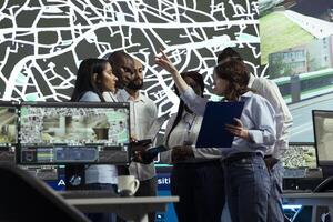 Group of diverse employees uniting forces to ensure express delivery, working on new routes to avoid urban traffic. Agency operating on CCTV surveillance system and satellite map tracking. photo
