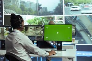 Indian specialist monitoring traffic surveillance next to a greenscreen display, gather intelligence on traffic activity in the city. Government employee collecting data on cars, plate recognition. photo