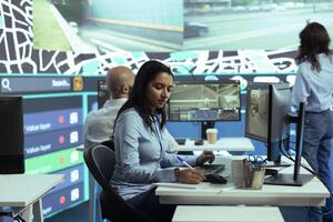 Indian woman employee locating delivery truck drivers via satellite map, sending gps coordinates for their destination to avoid traffic and ship orders faster. Operator studies CCTV footage. photo