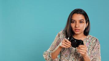 Cheerful woman playing videogames with controller, studio background. Indian gamer smiling, having fun by participating in PvP online multiplayer game using console system, camera B photo