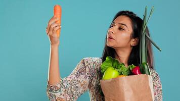 Woman with paper bag in hands filled with vegetables checking carrot for impurities. Conscious living customer with purchased groceries to be used as cooking ingredients, studio background, camera B photo