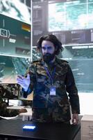 Army soldier examines real time data on a hologram 3d projection, reviewing defense operation details in military control room. Trooper looks at CCTV satellite footage on 3d visualization. photo