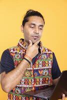 Pensive man thinking how to solve business tasks on laptop, isolated over studio background. Employee caught in brainstorming process, doing marketing analysis on notebook photo
