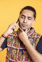 Man talks with friend over telephone call, doing stroking chin gesture. Pensive person talking with mate in phone call, thinking and processing information received, studio background photo