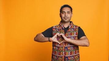 Portrait of smiling loving man doing heart symbol shape gesture with hands, showing kindness. Happy affectionate person doing tender love gesturing, isolated over studio background, camera B photo