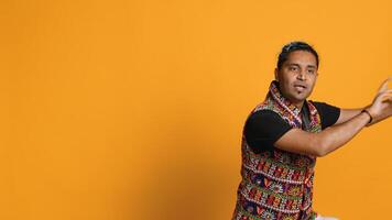 Ecstatic person wearing traditional indian attire doing energetic dance steps. Lively talented man doing entertaining bollywood choreography moves, studio background, camera A photo