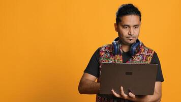 Indian man composing email, typing on laptop, frustrated with malfunctioning keyboard. Person sending mail online, struggling to use defective notebook, studio background, camera A photo