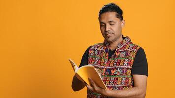 Indian man reading book, having fun and enjoying characters and plot, isolated over studio background. Relaxed person browsing novel, enjoying leisure time, appreciating literature, camera A photo