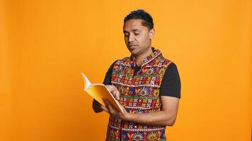 Indian man reading book, having fun and enjoying characters and plot, isolated over studio background. Relaxed person browsing novel, enjoying leisure time, appreciating literature, camera B photo