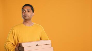 Portrait of courier isolated over studio background carrying stack of pizza boxes, close up shot. Indian employee delivering food waiting for client to answer door and pick up meal order, camera A photo