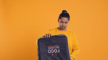 Delivery man doing face palm, shocked to see he displaced order in thermal backpack, throwing vegetables. Courier making mistake, packing incorrect groceries in bag, studio background, camera B photo