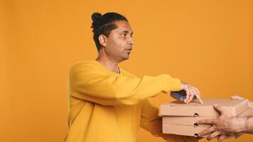 Pizza delivery man offering takeaway order to customer paying with credit card. Courier taking lunch boxes out of food backpack, giving POS to client to make transaction, studio background, camera A photo