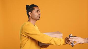 Indian delivery worker offering takeaway order to customer paying with debit card. Client buying meal from courier, swiping card on POS device, studio background, camera A photo