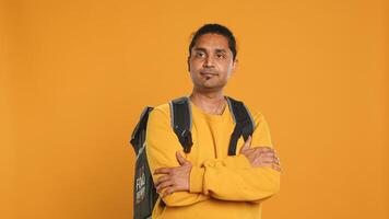 Portrait of confident indian man holding thermal backpack, crossing arms, studio background. Radiant nonchalant delivery person prepared to deliver takeaway food to customers, camera A photo