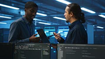 Engineers working in high tech server farm, using laptop and tablet to analyze data, ensuring seamless data flow. Men examining hardware in data center, ensuring system integrity and security photo
