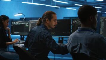 Multiracial coworkers in data center coding and checking parameters on computer. Multiethnic team working together, doing programming in high tech workspace, overseeing server clusters photo