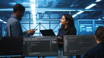 Technician and team leader in server farm looking for equipment misconfigurations affecting performance. Multiethnic coworkers checking data center infrastructure bottlenecks leading to glitches photo
