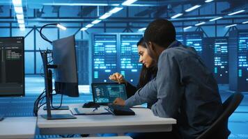 Multiethnic coworkers doing system analysis of server farm supercomputers using tablet. Diverse team of engineers looking at parameters in data center housing storage infrastructure photo