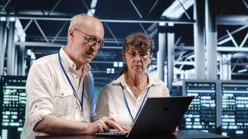 Octogenarian IT team looking around high tech data center, using laptop to crosscheck disaster recovery plan and assess server devices in need of replacement, preventing bugs photo