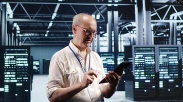 Octogenarian professional navigating network of server rigs in industrial base of operations. Admin with tablet doing review and optimizations in high tech data center, preventing system flaws photo