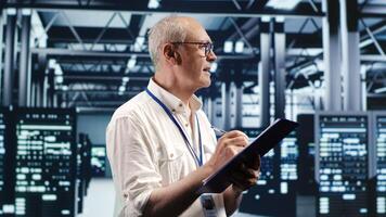 Elderly engineer looking around high tech data center, using clipboard to crosscheck disaster recovery plan and assess server components in need of replacement, preventing failures photo