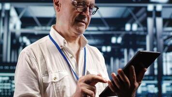 Productive professional navigating network of rigs in industrial data storage business center. Supervisor with tablet doing probing and optimizations in server room, preventing system liabilities photo