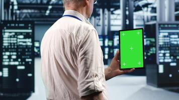 Technician in high tech data center using green screen tablet to monitor energy efficient servers using renewable sources employed to minimize consumption and reduce overall facility carbon footprint photo
