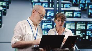 Focused IT inspectors looking around data center, using laptop and tablet to crosscheck disaster recovery plan and assess high tech establishment units in need of replacement, preventing perils photo