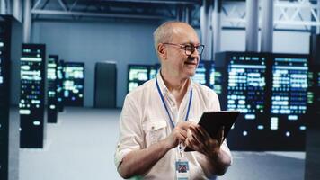 Senescent employee expertly managing data while navigating through industrial server rows. Octogenarian worker ensuring smooth cybersecurity protection, optimizing systems photo