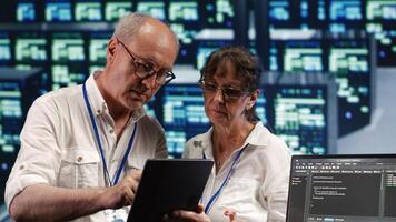 Tech savvy inspectors solving tasks on tablet while scripts are running on laptop terminal. Productive IT practitioners amidst servers, accessing databases and manipulating lines of code photo