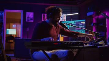 Sound engineer pressing keys of electric synthesizer and recording new music, adjusting noise level. Artist singing song on microphone, works with mixing board in home studio. Camera B. photo
