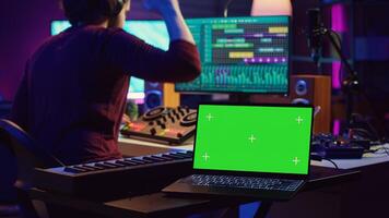 Music engineer editing audio recordings on mixing console and daw software, having a laptop with greenscreen in home studio. Artist producing a new song with acoustical engineering tools. Camera A. photo