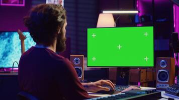 Music producer learning to use mixing console and soundboard, using online tutorial lesson on greenscreen. Artist learns to edit songs and add audio effects, mixing and mastering tracks. Camera A. photo