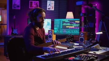 Musical composer recording his guitar tunes and adding piano key sounds, creating a beautiful song with mixing console and daw software. Sound engineer working with electronic tools. Camera B. photo