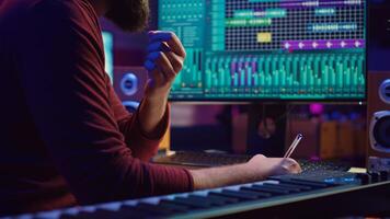 Songwriter creating a special song before recording tunes on musical instruments, writing down the words and melodic elements at his home studio. Artist producing sounds with DAW software. Camera A. photo
