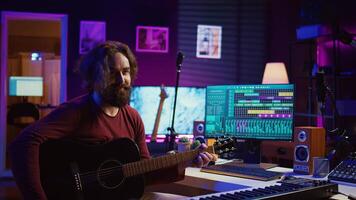 Young man songwriter playing guitar and creating music using equalizer program. Musician recording song in home studio, engineer mixing and mastering pop rock tracks. Camera B. photo