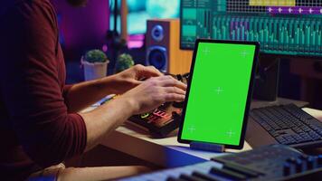 Music producer songwriter mixing tunes on stereo console, recording sounds next to tablet with greenscreen layout. Artist using equalizer and control panel board, daw software. Camera A. photo