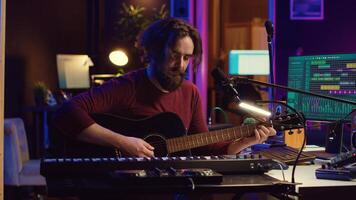 Music producer singing song and playing acoustic guitar, working in his personal home studio to record a new melody. Audio engineer recording tunes, editing with mixing console soundboard. Camera A. photo