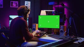 Music producer learning to use mixing console with online tutorial on computer, looking at isolated greenscreen display. Sound engineer practices editing sounds in his home studio. Camera B. photo