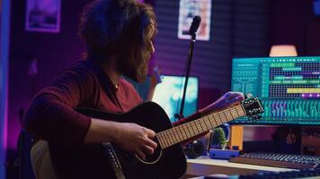 Music producer tuning his acoustic guitar before playing instrument, recording and mixing tunes to create new soundtracks. Singer composing a song using electronic panel controls. Camera B. photo